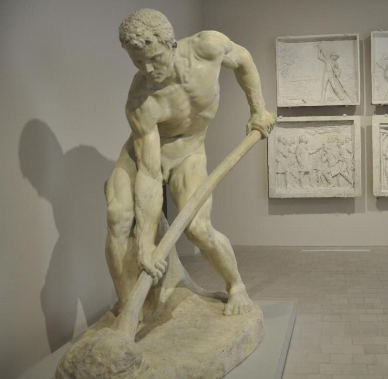 Intérieur d'un atelier de sculpture avec un artiste travaillant sur une sculpture de visage en argile, outils visibles.